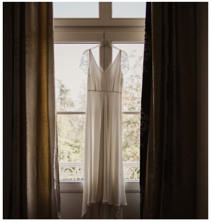 photo avec vue sur la fenêtre depuis la chambre des mariés, avec la robe de mariée blanche accrochée au centre de la fenêtre